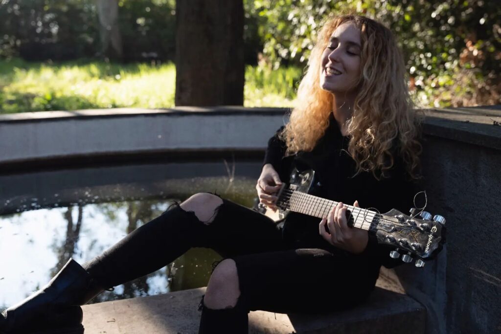 Vale sitzt mit einer Gitarre in der Hand an einem Brunnen in einem Park.
